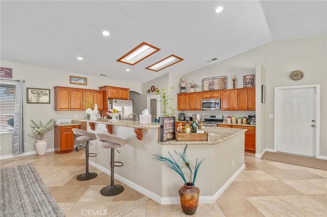 kitchen with appliances with stainless steel finishes, a center island with sink, light stone countertops, lofted ceiling, and a breakfast bar