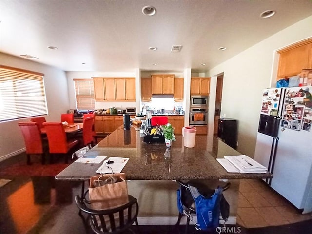 kitchen with appliances with stainless steel finishes, a kitchen breakfast bar, dark stone countertops, and dark tile patterned floors