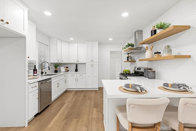 kitchen featuring stainless steel appliances, a breakfast bar, white cabinets, light countertops, and wall chimney range hood