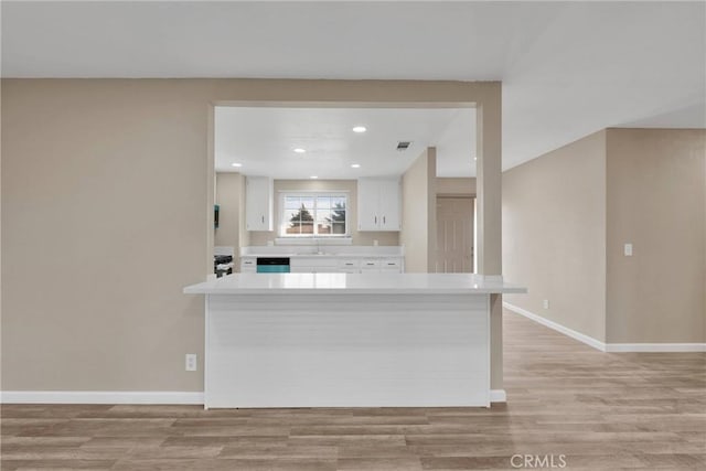 kitchen with baseboards, light countertops, a peninsula, and white cabinets