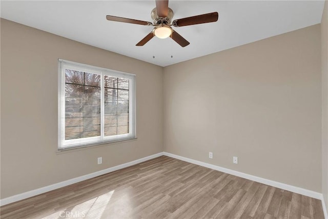 spare room featuring light wood finished floors, a ceiling fan, and baseboards