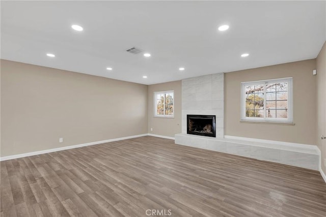 unfurnished living room featuring light wood-style flooring, a tile fireplace, visible vents, and baseboards