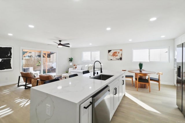 kitchen with stainless steel appliances, an island with sink, light stone countertops, white cabinets, and sink