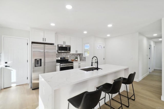 kitchen featuring appliances with stainless steel finishes, a kitchen island with sink, sink, white cabinetry, and a kitchen bar