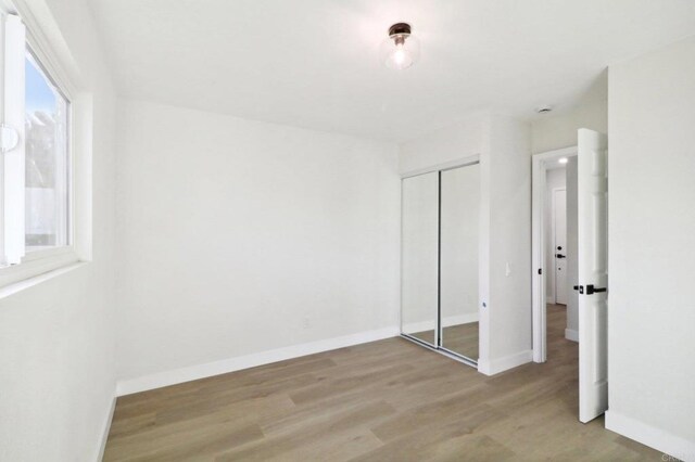 unfurnished bedroom featuring light hardwood / wood-style flooring, multiple windows, and a closet