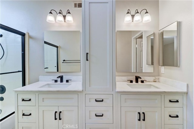 full bath featuring visible vents, a sink, double vanity, and shower / bath combination with glass door