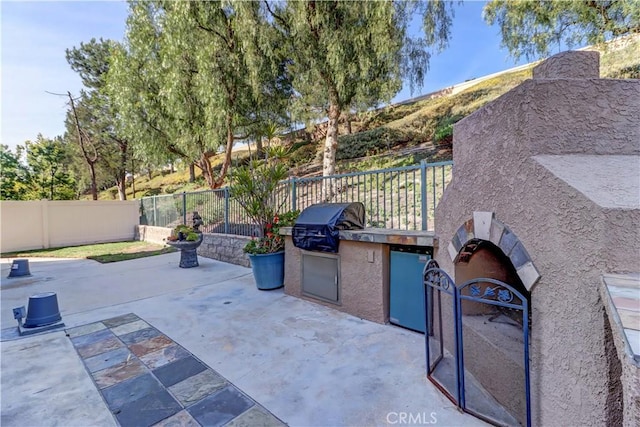 view of patio / terrace with a fenced backyard, exterior fireplace, and area for grilling