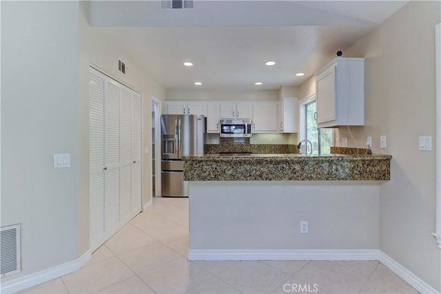 kitchen featuring dark stone counters, stainless steel appliances, visible vents, and white cabinetry