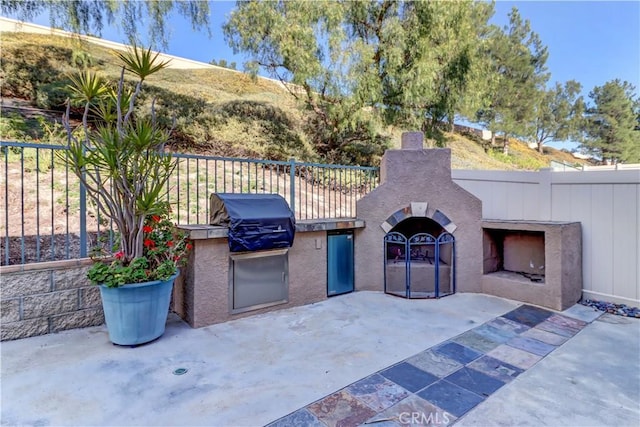 view of patio / terrace with grilling area, fence, an outdoor kitchen, and exterior fireplace