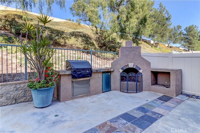 view of patio with exterior fireplace, fence, and area for grilling