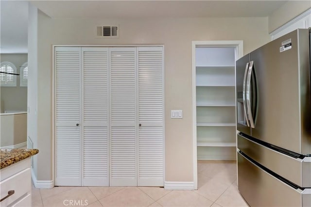 interior space featuring stainless steel refrigerator with ice dispenser, visible vents, light tile patterned floors, baseboards, and stone countertops