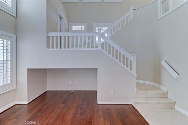 stairs featuring wood finished floors, a towering ceiling, and baseboards