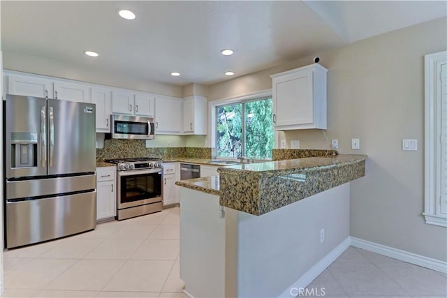 kitchen featuring light tile patterned floors, appliances with stainless steel finishes, stone countertops, white cabinets, and a peninsula