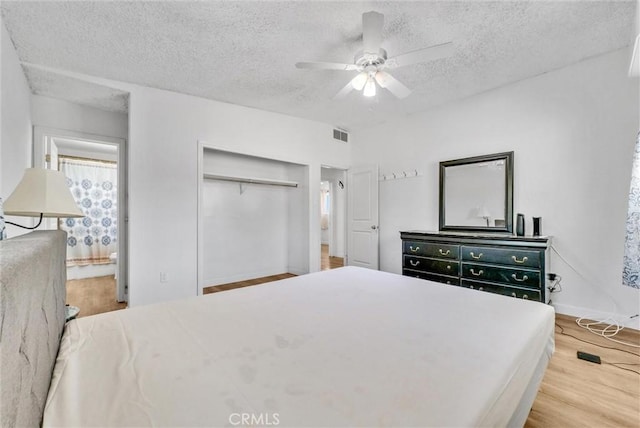 bedroom featuring ensuite bath, light hardwood / wood-style flooring, a closet, ceiling fan, and a textured ceiling