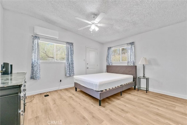 bedroom featuring vaulted ceiling, an AC wall unit, light wood-type flooring, a textured ceiling, and ceiling fan