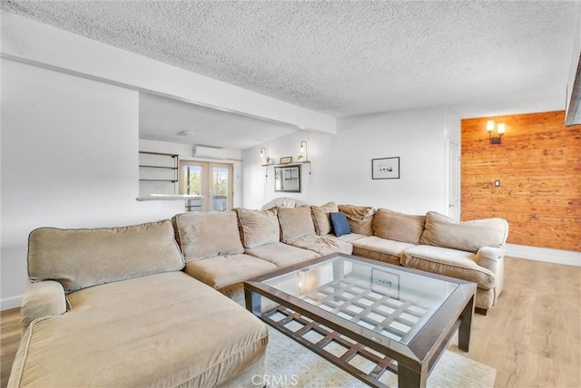 living room featuring french doors, beam ceiling, light hardwood / wood-style floors, a textured ceiling, and wooden walls