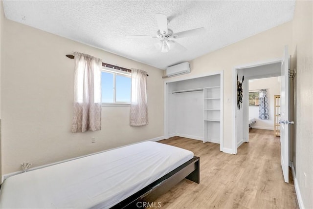 bedroom featuring a closet, a textured ceiling, ceiling fan, a wall mounted AC, and light wood-type flooring