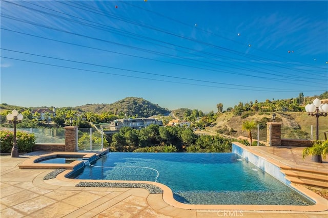 view of pool with a patio, an in ground hot tub, a mountain view, and pool water feature