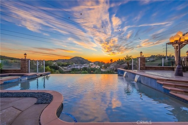 pool at dusk with a mountain view, a patio, and pool water feature