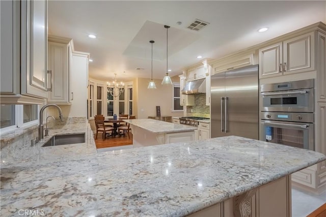 kitchen with sink, pendant lighting, stainless steel appliances, light stone countertops, and cream cabinets