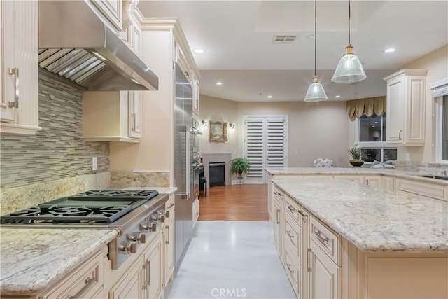 kitchen featuring pendant lighting, cream cabinetry, a kitchen island, a fireplace, and stainless steel gas stovetop