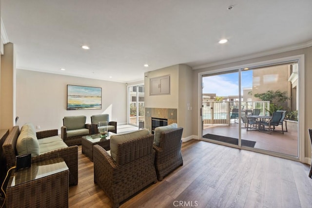 living area with a tile fireplace, recessed lighting, wood finished floors, and crown molding