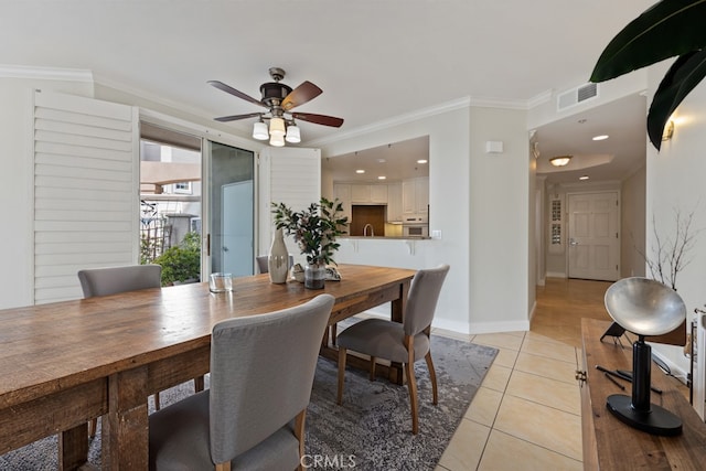 dining room with light tile patterned floors, baseboards, visible vents, a ceiling fan, and ornamental molding