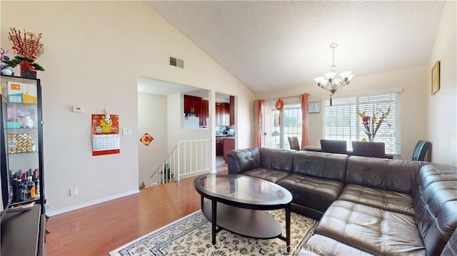 living area with visible vents, vaulted ceiling, wood finished floors, a chandelier, and baseboards