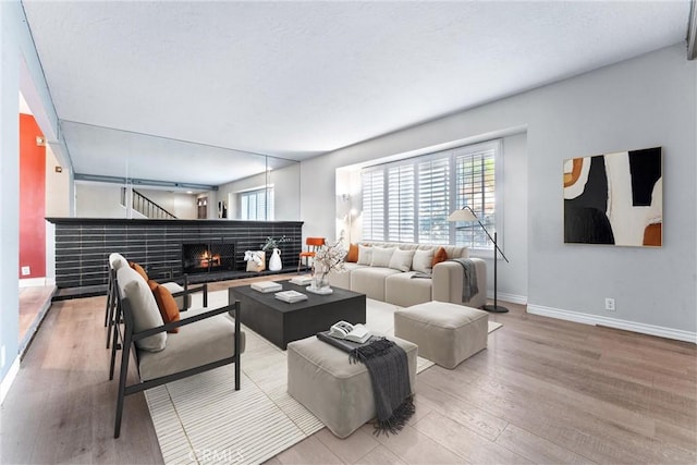 living area featuring light wood-style flooring, a lit fireplace, and baseboards