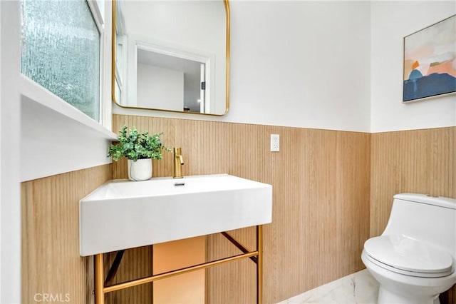 bathroom featuring toilet, marble finish floor, and wainscoting