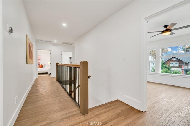 corridor with visible vents, baseboards, an upstairs landing, and light wood-style floors