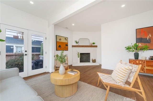 living room featuring recessed lighting, a fireplace with raised hearth, wood finished floors, and french doors