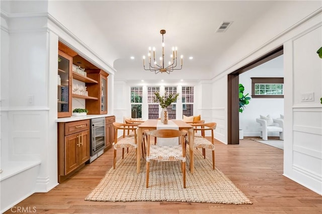 dining area with light wood finished floors, beverage cooler, visible vents, an inviting chandelier, and a decorative wall