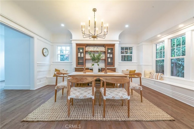 dining area featuring a wainscoted wall, dark wood finished floors, a decorative wall, and a notable chandelier