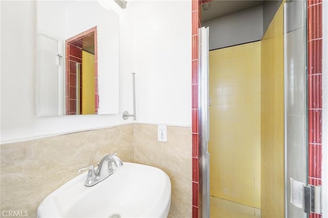 bathroom with a tile shower, a sink, and tile walls