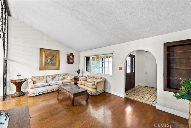 living area featuring arched walkways, lofted ceiling, a textured ceiling, wood finished floors, and baseboards