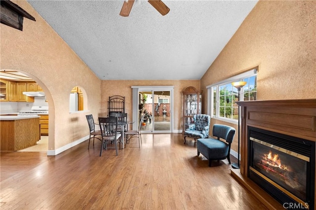 sitting room featuring a textured ceiling, a textured wall, wood finished floors, baseboards, and a glass covered fireplace