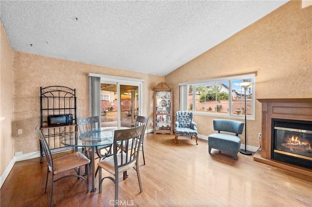 dining area featuring vaulted ceiling, wood finished floors, a glass covered fireplace, and baseboards