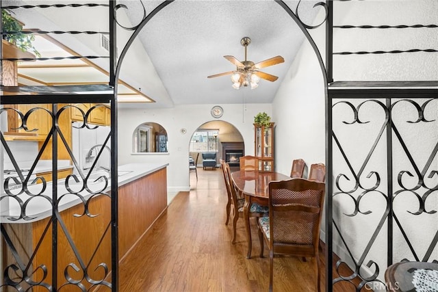 dining area with arched walkways, ceiling fan, a textured ceiling, lofted ceiling, and wood finished floors