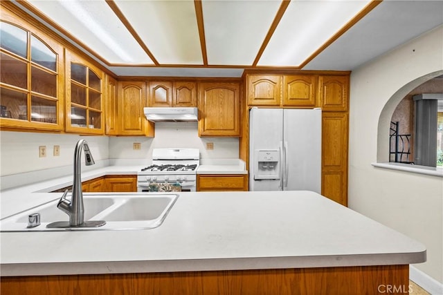 kitchen featuring white appliances, brown cabinets, a sink, and under cabinet range hood