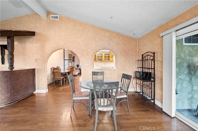 dining space featuring vaulted ceiling with beams, visible vents, arched walkways, and wood finished floors