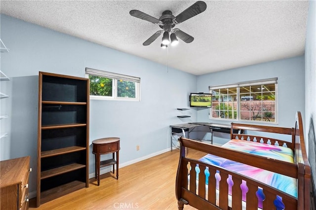 bedroom with a ceiling fan, light wood-style flooring, baseboards, and a textured ceiling