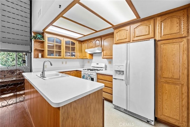 kitchen with under cabinet range hood, a peninsula, white appliances, a sink, and glass insert cabinets