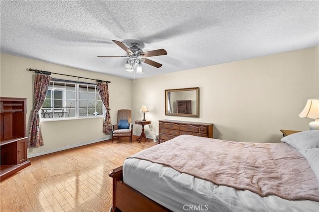 bedroom with hardwood / wood-style flooring, a textured ceiling, baseboards, and a ceiling fan