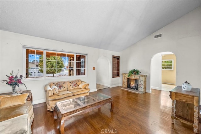 living area with arched walkways, visible vents, vaulted ceiling, wood finished floors, and a lit fireplace