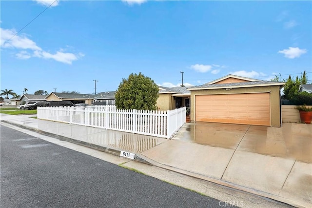 ranch-style home featuring a fenced front yard, driveway, an attached garage, and stucco siding