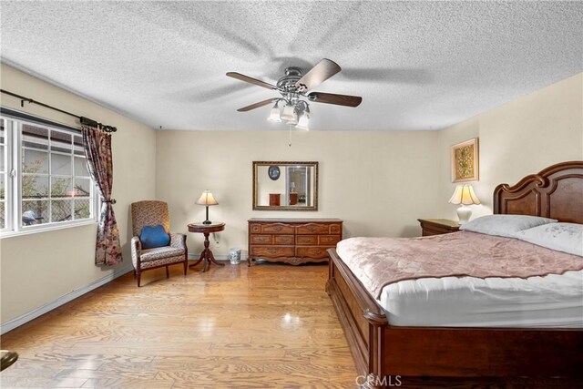 bedroom with light wood finished floors, a ceiling fan, baseboards, and a textured ceiling