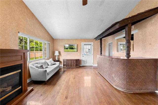 living area with a textured wall, a glass covered fireplace, vaulted ceiling, a textured ceiling, and wood finished floors