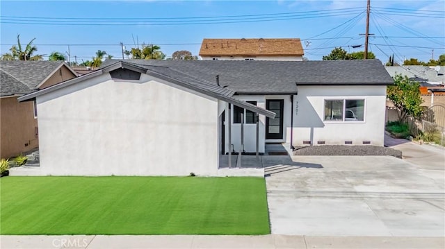 view of front facade with a patio, stucco siding, a shingled roof, a front yard, and fence