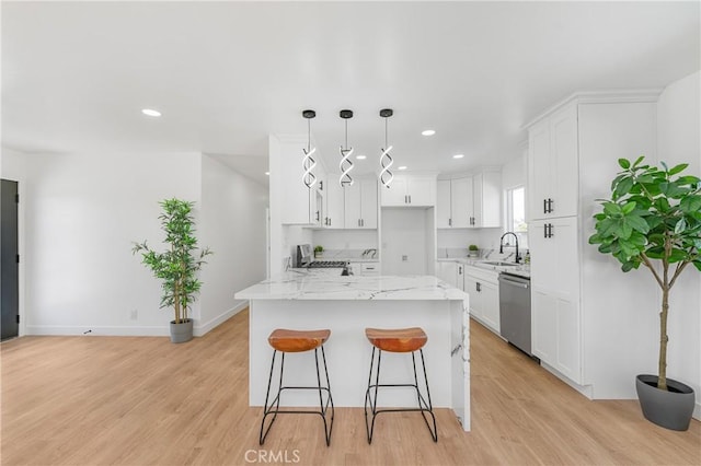 kitchen with a sink, white cabinets, stainless steel dishwasher, light stone countertops, and decorative light fixtures